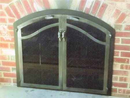 Osterville Arch With Horizon Wave Design Black frame finish, natural iron vice bi fold doors. standard smoked glass. Customer Center handles, no mesh, no draft panel. Installed on brick.